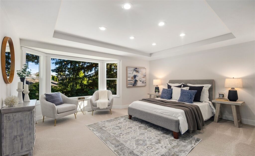 Primary suite with a tray ceiling, upholstered bed and sitting area in a staged Newcastle home