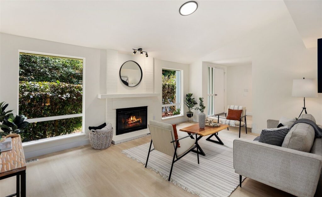 Seating area arranged around a fireplace with a round mirror and garden views